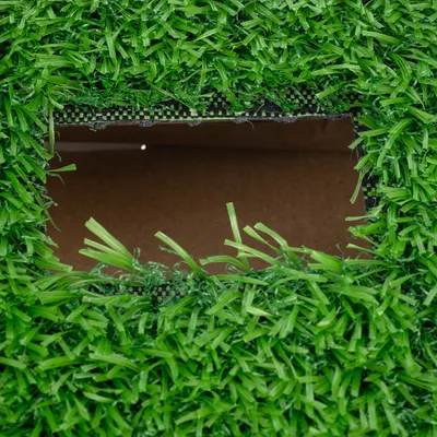 Close-up of a rectangular section in green artificial turf with visible brown cardboard underneath.