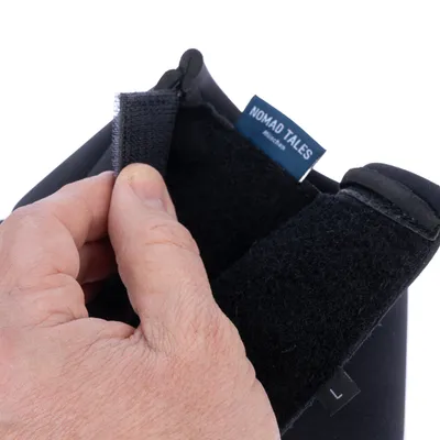 Nahaufnahme einer Hand, die den Klettverschluss eines schwarzen Produkts öffnet. Sichtbar ist das Etikett mit der Aufschrift 'Nomad Tales'.