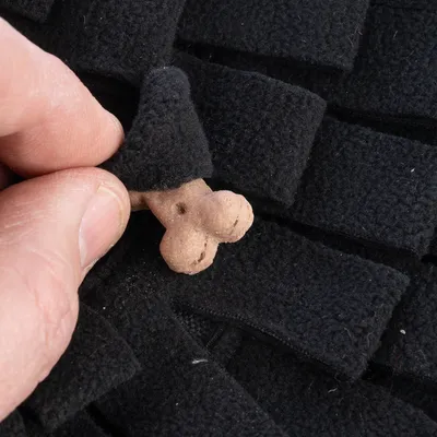 Mano estrae un piccolo osso per cani da un tappeto olfattivo nero. Prodotto per l'intrattenimento e la ricompensa degli pet.