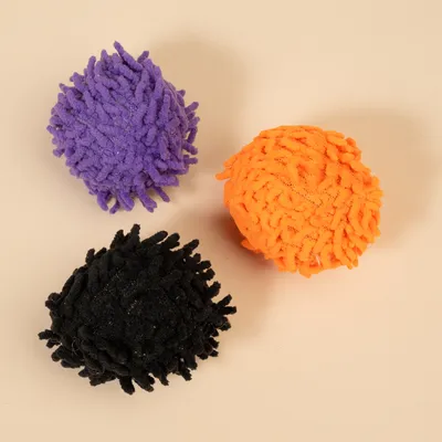 Tre palline da gioco soffici nei colori viola, arancione e nero su sfondo beige.