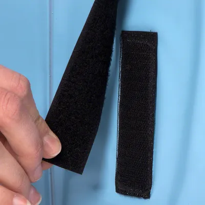 Primer plano de cierre de velcro negro abierto con una mano. Muestra la función del cierre sobre fondo azul.