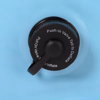Válvula negra con inscripción: 'Push-in Valve Tab to Deflate' y 'Pull On Valve to Inflate' sobre fondo azul claro.