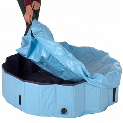 Piscina azul plegable para perros con cubierta, persona muestra la facilidad de uso al abrir. Válvula de drenaje visible en el lateral.