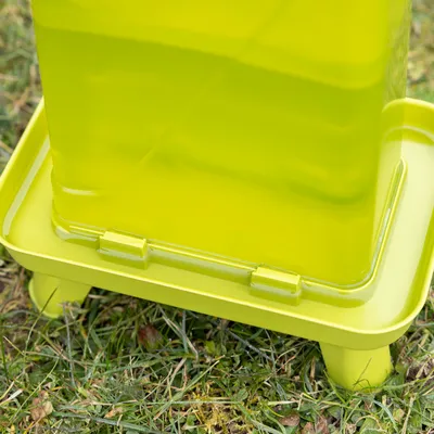 Green plastic container with raised base, suitable for outdoor use on grass.