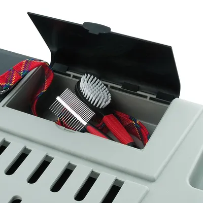 Opbergvak van kunststof transportbox met open klep, zichtbaar: rood handvat borstel, metalen kam en gekleurde riem.