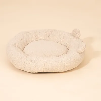 Rundes, cremefarbenes Bett aus weichem Plüschmaterial mit zwei kleinen Ohren an der Seite. Rundes, cremefarbenes Bett aus weichem Plüschmaterial mit zwei kleinen Ohren an der Seite.