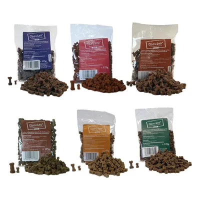 6 sachets de friandises Chewies 125 g, différents parfums visibles sur les étiquettes colorées, friandises en forme d’os devant chaque sachet. Texte principal en allemand.