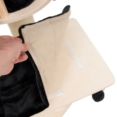 Afneembaar zwart-beige kussen van stof op houten kattenmeubel, bevestigd met klittenband. Hand toont het losmaken van het kussen.