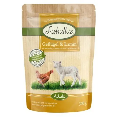 Confezione Lukullus Geflügel & Lamm, testo visibile: Adult, 300 g. Immagine di una gallina e un agnello sull'erba. Testo in inglese: Poultry & Lamb with potatoes, dandelion and grape seed oil.