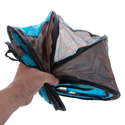 Zusammengefaltetes tragbares Netzgehege mit blauem und braunem Stoff, gehalten in einer Hand.