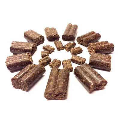 Friandises brunes en forme de bâtonnets coupés, disposées en cercle sur fond blanc. Aucun emballage ou texte visible.