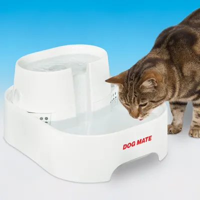 Fântână de apă albă DOG MATE, cu două niveluri, utilizată de o pisică care bea apă. Logo-ul DOG MATE este vizibil pe partea frontală a fântânii.