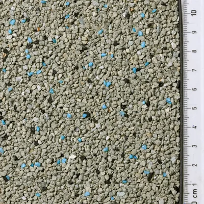 Nahaufnahme von grauem Katzenstreu mit blauen Körnern, Maßstab in Zentimetern sichtbar rechts im Bild.