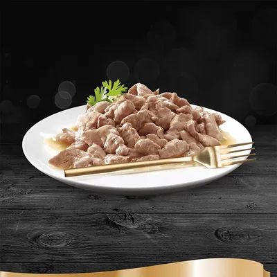 Hvid tallerken med stykker af vådfoder i sovs, pyntet med et grønt blad og en gylden gaffel ved siden af. Ingen synlige mærker eller tekst.