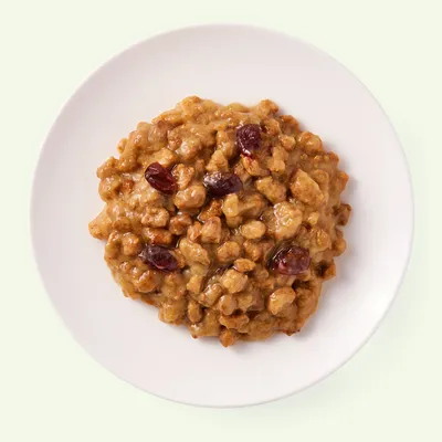 Portie natvoer met stukjes vlees en enkele rode bessen op een wit bord, zonder zichtbare verpakking of merknaam.