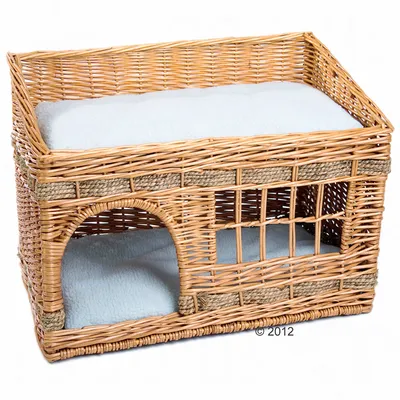 Braided basket with two levels, lower level with entrance and upper level with white cushion. Made of rattan.