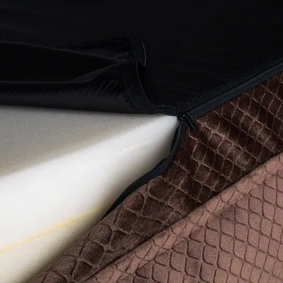 Husă cu fermoar deschis, arătând strat de spumă albă și material textil maro cu model. Fermoarul este negru, iar partea superioară a husei pare din material sintetic.