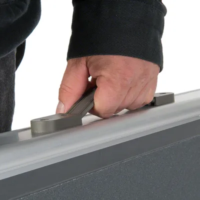 Hand houdt een grijze kunststof handgreep van een transportbox of koffer vast. Alleen het handvat en een deel van de box zijn zichtbaar.