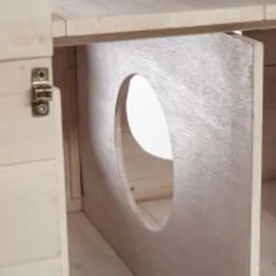 Indvendig del af træbur med metalbeslag og rund åbning i skillevæg, lyst træmateriale synligt.