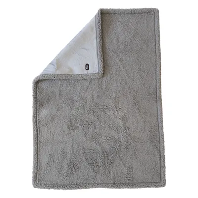 Couverture grise en tissu doux, forme rectangulaire, coin replié montrant l’étiquette noire avec texte blanc « TIAKI » visible.