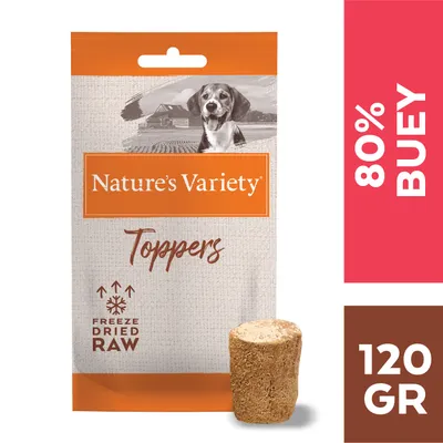 Bolsa de Nature’s Variety Toppers, texto visible: 80% buey, 120 gr, Freeze Dried Raw. Imagen de un perro y una pieza del producto delante del envase.
