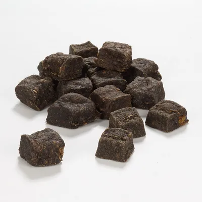 Morceaux cubiques de friandises brunes pour animaux, disposés en tas sur fond blanc. Aucun emballage ni marque visible.