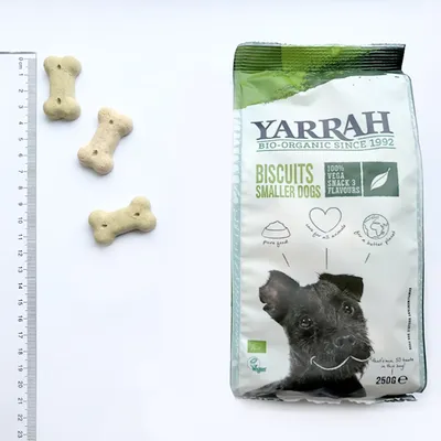 Yarrah Biscuits Smaller Dogs 250 g -pussi, teksti: 100% Vega Snack 3 Flavours. Kolme luunmuotoista keksiä viivottimen vieressä mittaamista varten.