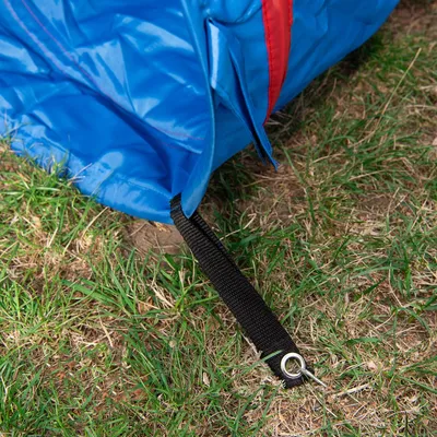 Sininen muovimateriaalia oleva tuote, jossa musta kiinnitysnauha ja metallinen rengas maassa nurmikolla. Punainen sauma näkyvissä.