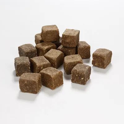 Morceaux cubiques de nourriture pour animaux, couleur brune, posés sur une surface blanche. Aucun emballage ou marque visible.