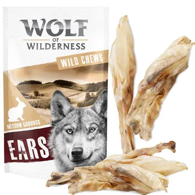Wolf of Wilderness Wild Chews Ears Meadow Grounds pack with wolf image, rabbit icon and visible dried animal ears beside packaging. Text: EARS, WILD CHEWS, MEADOW GROUNDS.