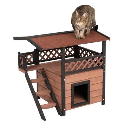 Træ-kattehus med trappe, overdækket balkon og rødt tag. Kat står på taget.