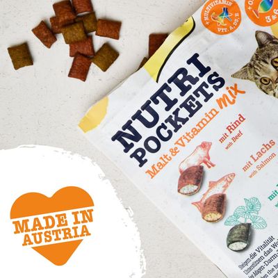 Nutri Pockets Malt & Vitamin Mix med texten 'mit Rind', 'mit Lachs' och hjärtsymbol med texten MADE IN AUSTRIA. Flera bitar av kattgodis synliga.