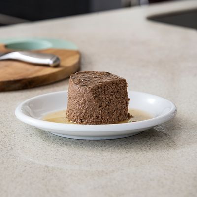 Porzione di cibo umido su un piatto bianco, servita con salsa. Sullo sfondo piano cucina e tagliere.