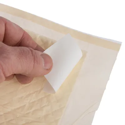 Una mano muestra cómo retirar una lámina protectora de una superficie adhesiva, apta para uso en productos.