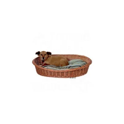 Perro marrón tumbado en una cama ovalada de mimbre con cojín a rayas grises y verdes. La cama está sobre fondo blanco.