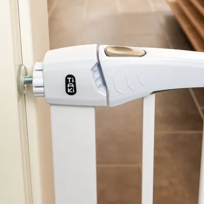 Tiaki barriera per porte con meccanismo di chiusura bianco, fissata a uno stipite. Vista dettagliata del sistema di bloccaggio.