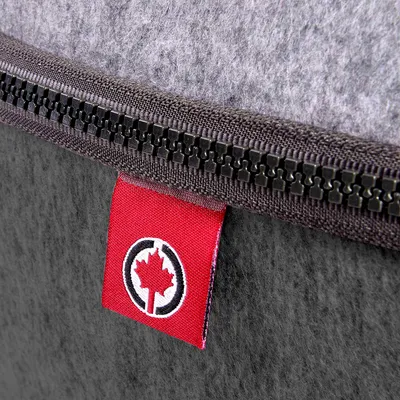 Czerwony materiałowy brelok z symbolem liścia klonu i czarnym okręgiem, przymocowany do szarego filcu z czarnym zamkiem błyskawicznym.
