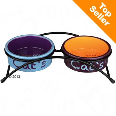 Deux gamelles en céramique colorées avec support métallique, texte visible : "Cat's" sur chaque bol. Étiquette orange en haut à droite : Top Seller.