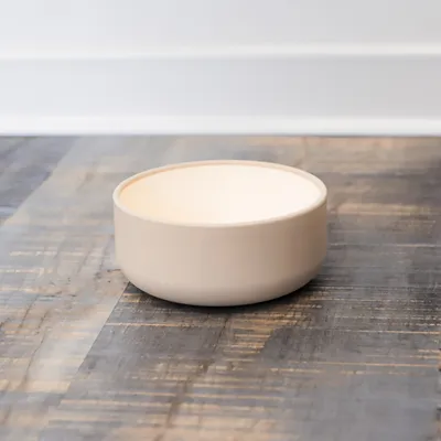 Beige Futternapf aus Keramik auf Holzoberfläche, geeignet für Haustierfutter oder Wasser.