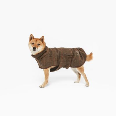 Chien portant un manteau marron en tissu, coupe couvrante avec fermeture sur le dos et logo brodé visible sur le côté.