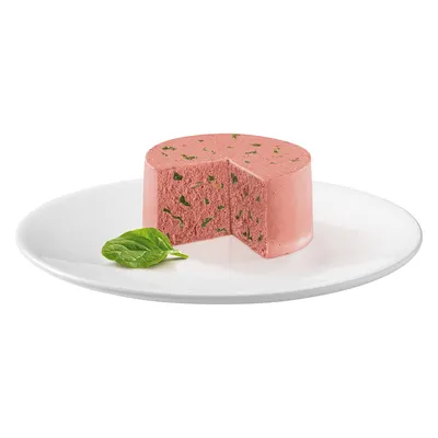 Rosa kødpate med grønne krydderurter, serveret på en hvid tallerken, pyntet med et frisk basilikumblad.