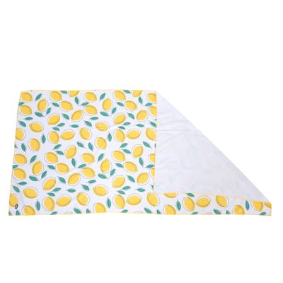 Tapis rectangulaire en tissu blanc avec motif de citrons jaunes et feuilles vertes, un coin replié montrant le revers uni blanc. Aucun texte ou marque visible.