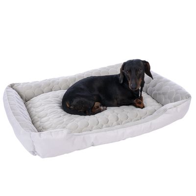 Hund liegt auf einem gepolsterten, hellgrauen Hundebett mit ovalem Muster.