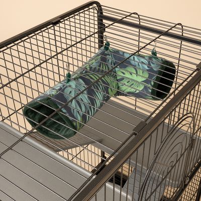Hängande tunnel av grön textil med bladmönster, fäst vid metallbur med krokar. Passar som lek- eller viloplats för smådjur.