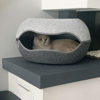 Letto per gatti grigio in feltro con apertura ovale, il gatto è sdraiato all'interno su una superficie rialzata.