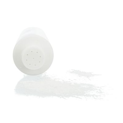 Barattolo di plastica bianca con fori sul tappo, rovesciato e con polvere bianca versata accanto. Nessun marchio o testo visibile.