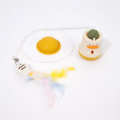 Juego de juguetes con media esfera amarilla, recipiente blanco y amarillo con cara de pato y pelota verde, además de colgante de plumas en una cuerda.