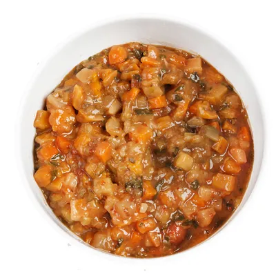 Close-up of a bowl with moist pet food, consisting of vegetable cubes and meat pieces in gravy.