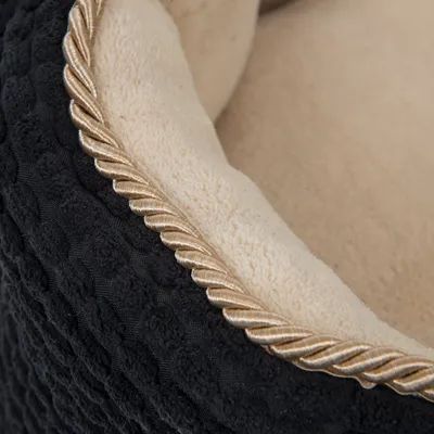 Gros plan sur le bord d’un panier pour animal en tissu noir à motif relief et intérieur beige doux, finition corde décorative dorée visible.