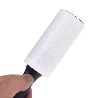 Hand håller en luddroller med svart handtag och vit klibbig yta, lämplig för att ta bort djurhår eller damm.